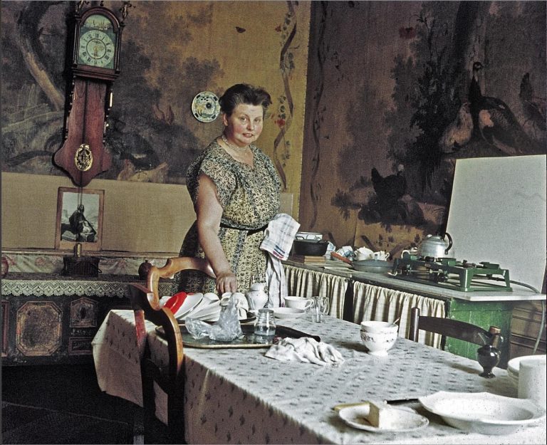 Een mevrouw in de keuken van een oud landhuis dekt de tafel.